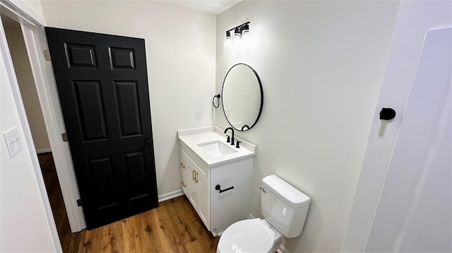 half bathroom featuring toilet, wood finished floors, and vanity