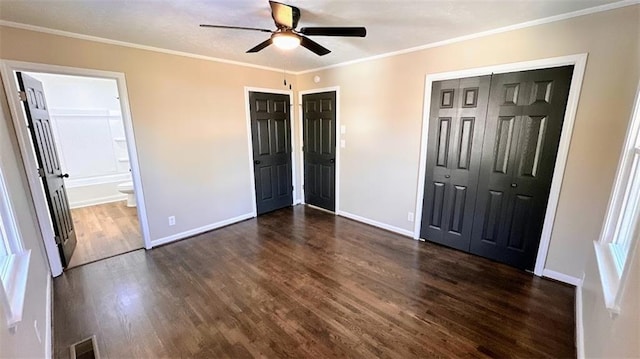 unfurnished bedroom featuring visible vents, dark wood-type flooring, baseboards, ornamental molding, and ensuite bath