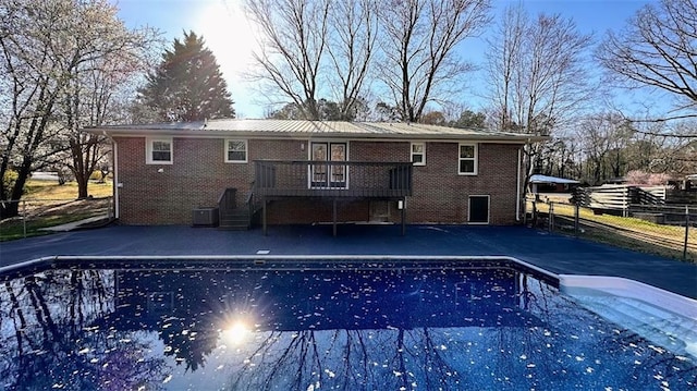 rear view of property with an outdoor pool, a wooden deck, and brick siding