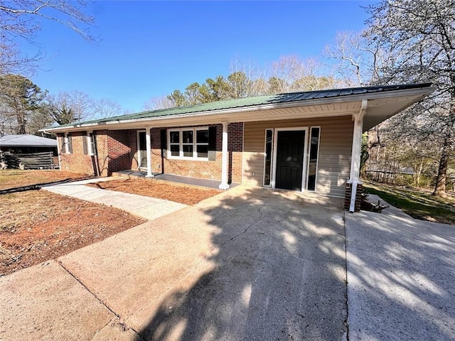 ranch-style home featuring concrete driveway, brick siding, and metal roof