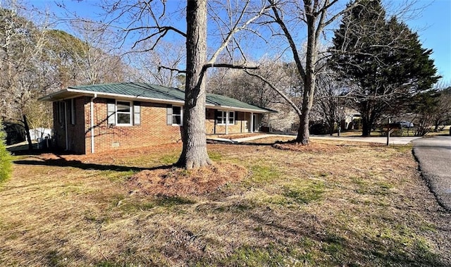 view of side of property with crawl space, brick siding, metal roof, and a yard