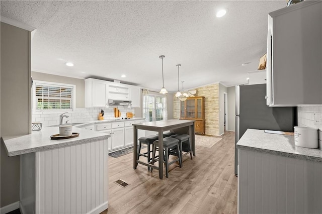 kitchen with ornamental molding, light wood-type flooring, hanging light fixtures, decorative backsplash, and white cabinets