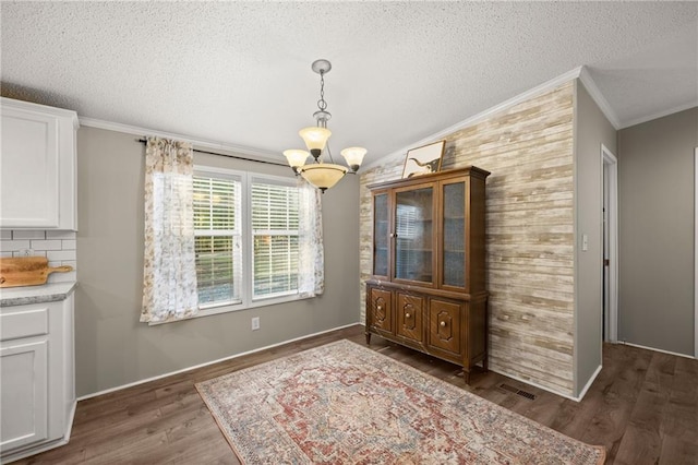 unfurnished dining area with dark wood-type flooring, a chandelier, a textured ceiling, and crown molding