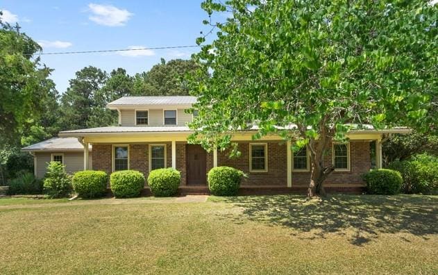 view of front facade with covered porch, brick siding, and a front yard