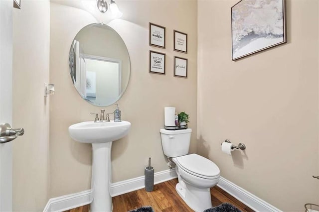 half bath with wood finished floors, toilet, and baseboards