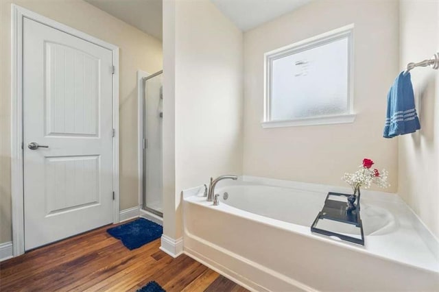 bathroom with baseboards, a shower stall, a bath, and wood finished floors