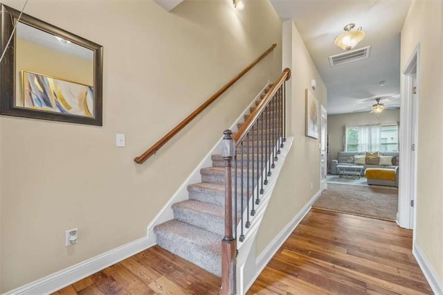 stairway with a ceiling fan, visible vents, baseboards, and wood finished floors