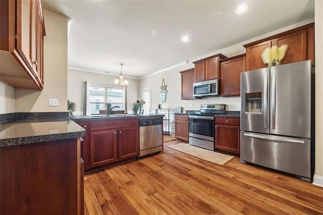 kitchen with appliances with stainless steel finishes, wood finished floors, a peninsula, crown molding, and a sink