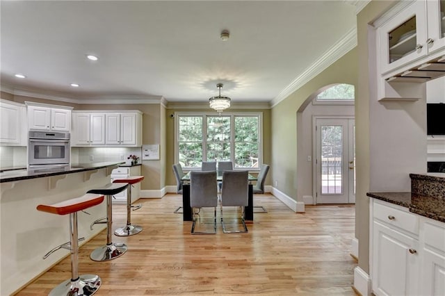 12130 Helleri Holw, Alpharetta, GA 30005 - kitchen featuring oven, a breakfast bar, white cabinetry, light wood-style floors, and arched walkways