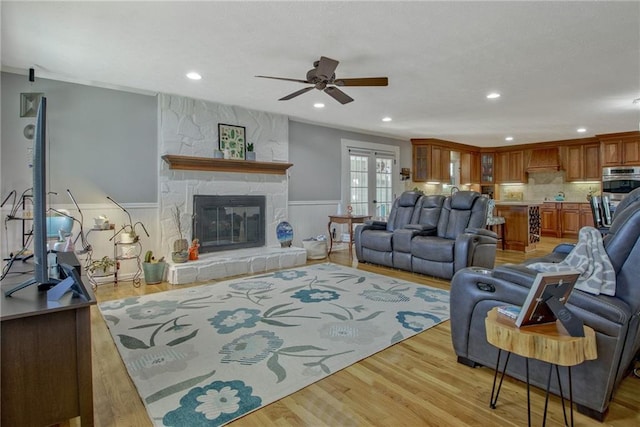 living room featuring ceiling fan, french doors, a stone fireplace, and light wood-type flooring