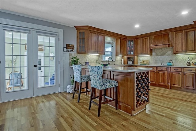 kitchen with custom exhaust hood, light hardwood / wood-style floors, a breakfast bar, and french doors