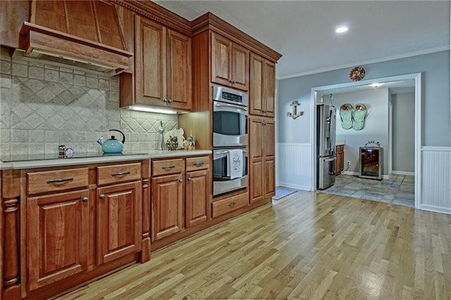 kitchen with appliances with stainless steel finishes, wine cooler, premium range hood, backsplash, and light wood-type flooring