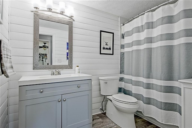 bathroom with vanity, toilet, wooden walls, and a textured ceiling