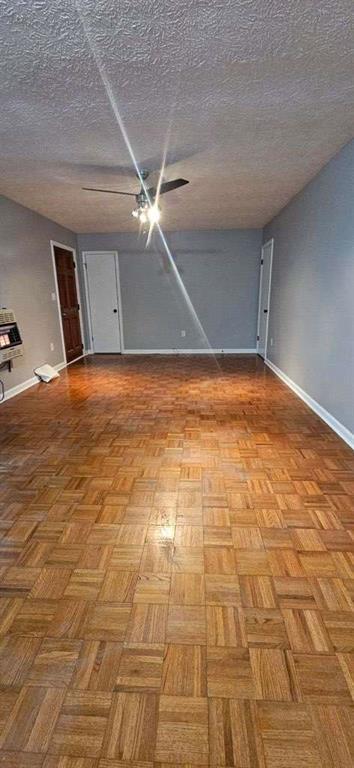 spare room with heating unit, ceiling fan, light parquet flooring, and a textured ceiling