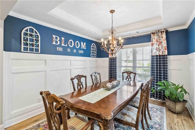 dining space with a raised ceiling, crown molding, hardwood / wood-style floors, and an inviting chandelier