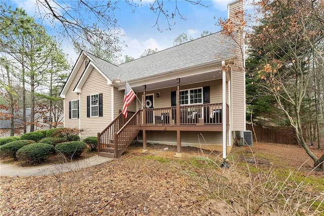 view of front facade featuring central AC, fence, covered porch, a shingled roof, and a chimney