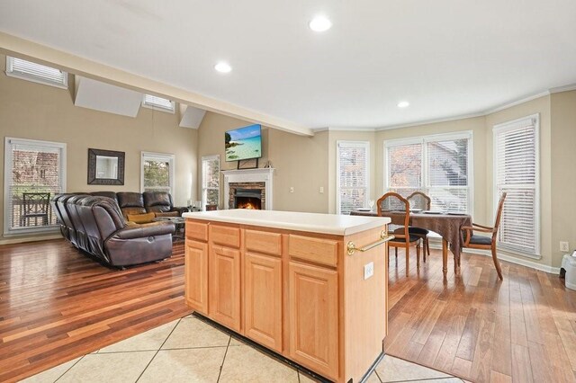 kitchen with a stone fireplace, crown molding, light hardwood / wood-style flooring, a kitchen island, and lofted ceiling