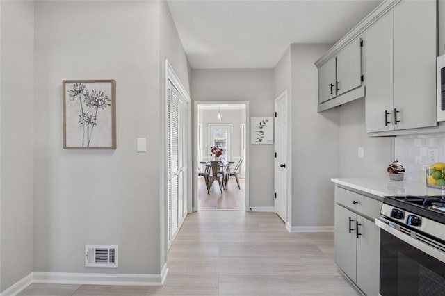 kitchen featuring stainless steel range with gas cooktop, gray cabinets, light countertops, visible vents, and baseboards