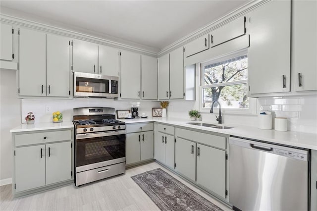 kitchen with a sink, light countertops, appliances with stainless steel finishes, gray cabinets, and decorative backsplash