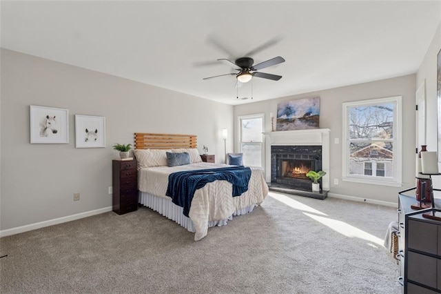 bedroom featuring carpet floors, a warm lit fireplace, ceiling fan, and baseboards