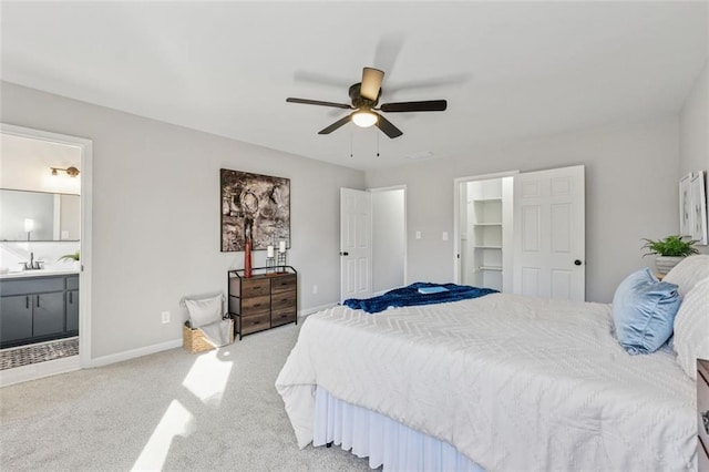 carpeted bedroom featuring a spacious closet, ensuite bathroom, ceiling fan, a sink, and baseboards