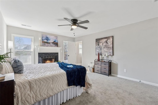 carpeted bedroom with a lit fireplace, a ceiling fan, visible vents, and baseboards