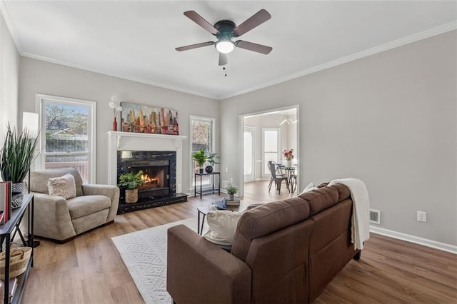 living room with a premium fireplace, ornamental molding, a ceiling fan, wood finished floors, and baseboards