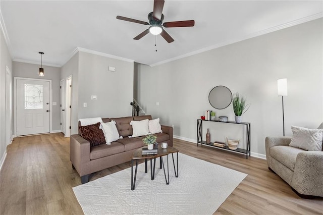 living area featuring light wood-style floors, a ceiling fan, baseboards, and crown molding