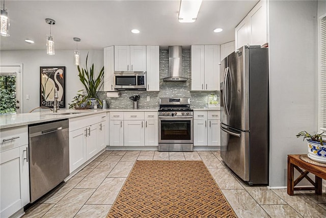 kitchen featuring hanging light fixtures, stainless steel appliances, wall chimney range hood, backsplash, and white cabinets