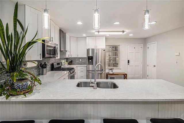 kitchen featuring sink, hanging light fixtures, wall chimney exhaust hood, white cabinetry, and stainless steel appliances