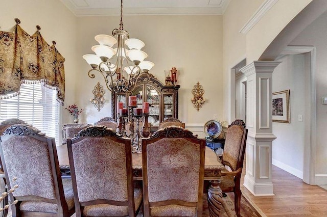 dining room featuring hardwood / wood-style floors, decorative columns, an inviting chandelier, and crown molding