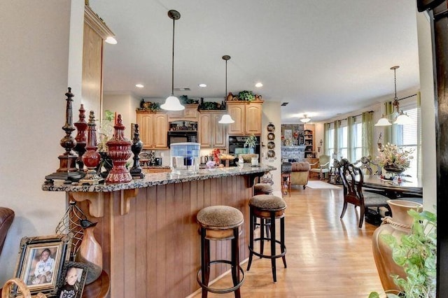 kitchen featuring light stone countertops, light hardwood / wood-style flooring, kitchen peninsula, a breakfast bar area, and black appliances