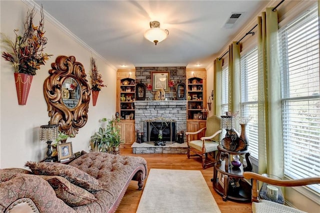 living room with built in shelves, a stone fireplace, light wood-type flooring, and ornamental molding