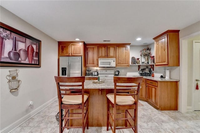 kitchen with a kitchen bar, light stone countertops, a center island, and white appliances