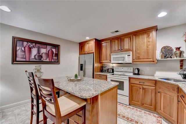 kitchen featuring light stone countertops, white appliances, a breakfast bar area, and sink