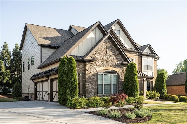 tudor home featuring board and batten siding, driveway, an attached garage, a shingled roof, and stone siding