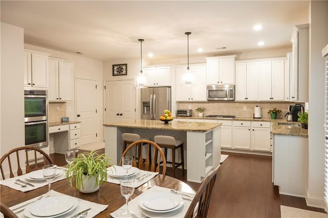 kitchen featuring dark wood-style floors, appliances with stainless steel finishes, decorative backsplash, and a center island