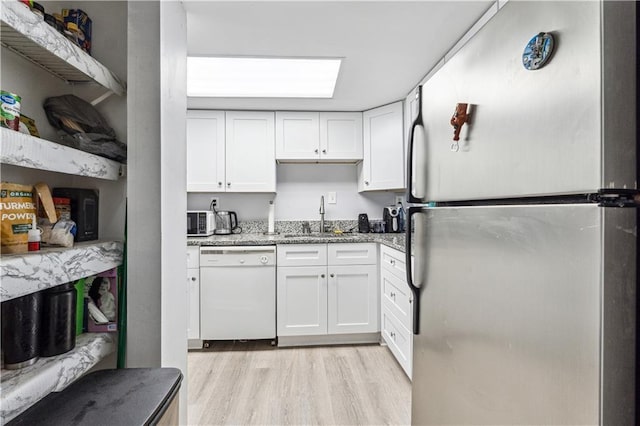 kitchen featuring stainless steel refrigerator, white cabinetry, dishwasher, sink, and stone countertops