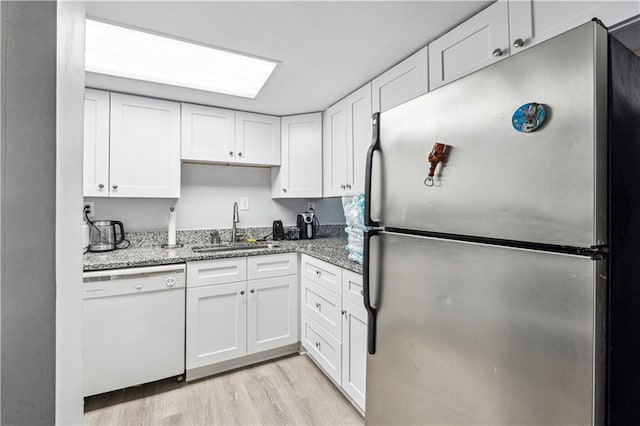 kitchen with dishwasher, white cabinets, sink, stainless steel fridge, and stone countertops