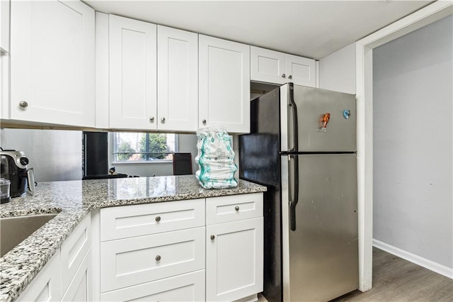 kitchen with white cabinets, stainless steel fridge, light hardwood / wood-style floors, and light stone counters