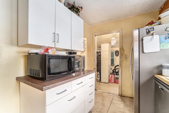 kitchen featuring dark countertops, light tile patterned floors, appliances with stainless steel finishes, and white cabinets