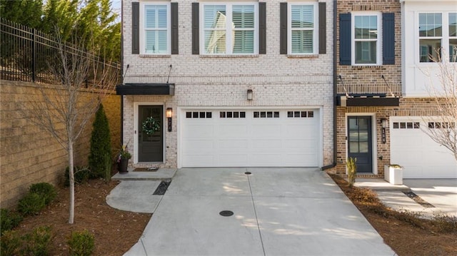 view of property with brick siding, an attached garage, concrete driveway, and fence