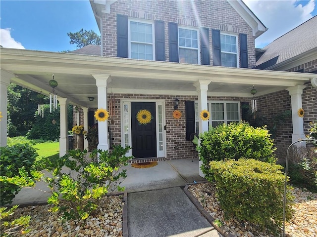 view of exterior entry with a porch and brick siding