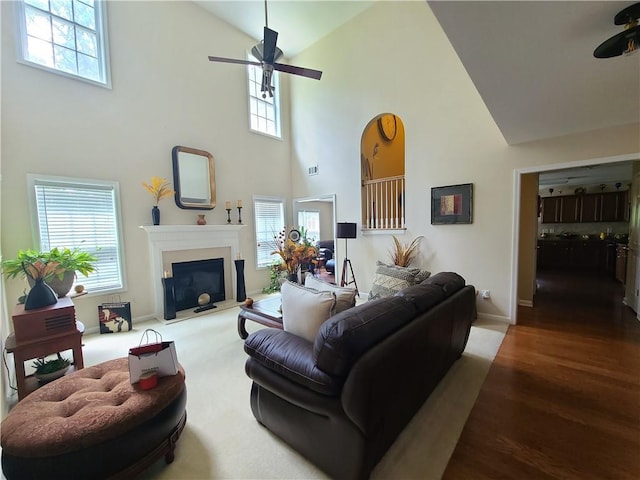 living area featuring a glass covered fireplace, wood finished floors, plenty of natural light, and ceiling fan