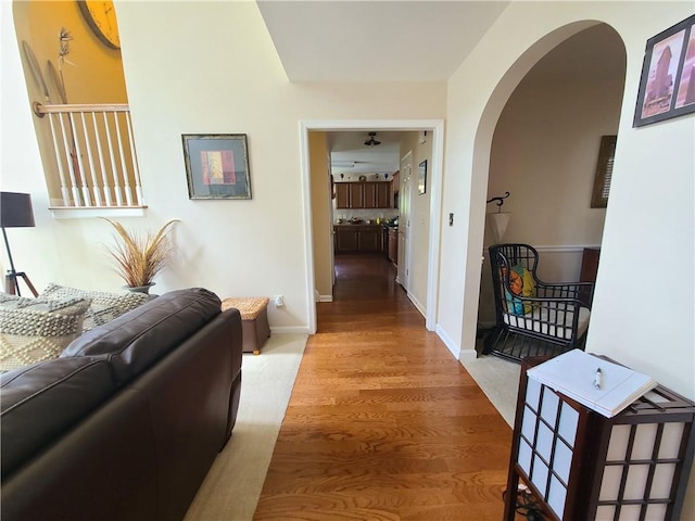 corridor with baseboards, arched walkways, and wood finished floors