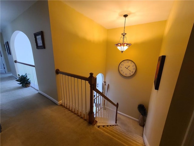 staircase with arched walkways, carpet floors, and baseboards