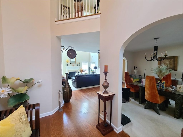 foyer with arched walkways, a fireplace, a towering ceiling, wood finished floors, and baseboards