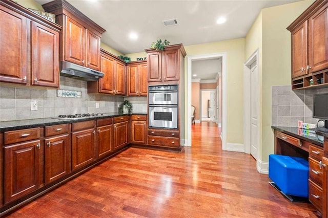 kitchen with hardwood / wood-style floors, backsplash, stainless steel appliances, and dark stone counters