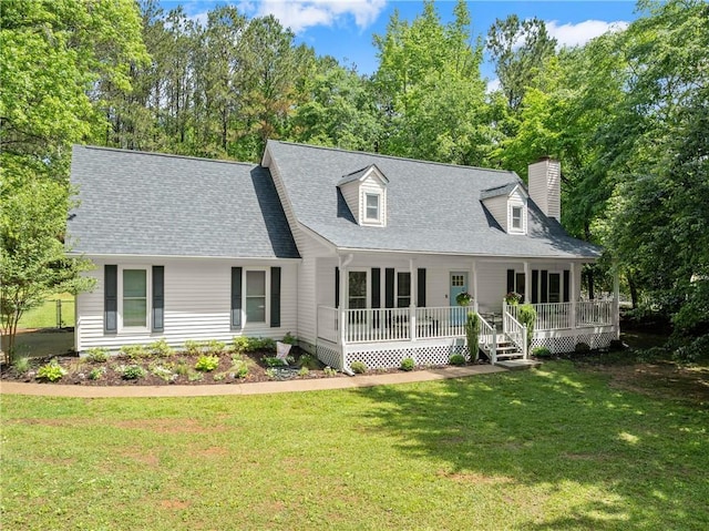 cape cod home with a porch, a front yard, a chimney, a shingled roof, and view of wooded area