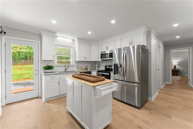 kitchen with stainless steel appliances, a sink, ornamental molding, white cabinets, and tasteful backsplash